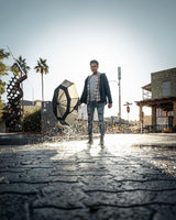 Man in a plaza holds an umbrella, facing the camera with the sun behind him.